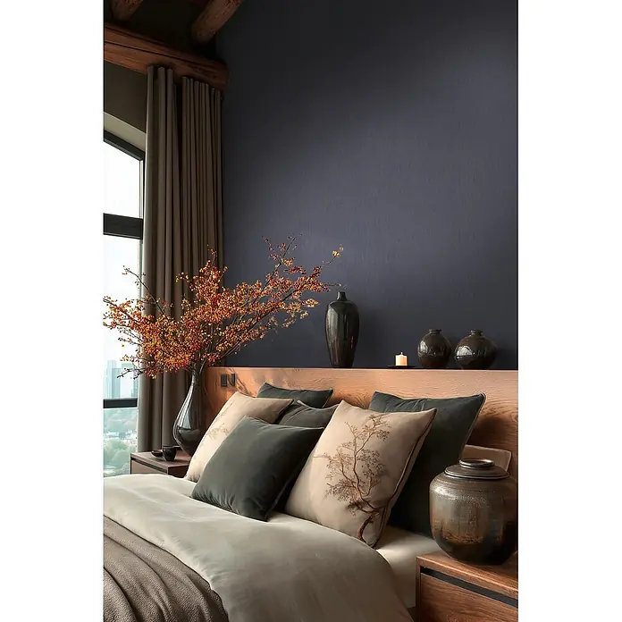 A.S. Création Metropolitan Stories Vibes & Styles Vliestapete Uni III - Blau-Dunkelgrau, Uni, 10,05 x 0,53 m - Ein Bett mit warm getönter Bettwäsche und Zierkissen, teils mit feiner Baumbestickung, in einem ruhigen Schlafzimmer mit Holzakzenten.