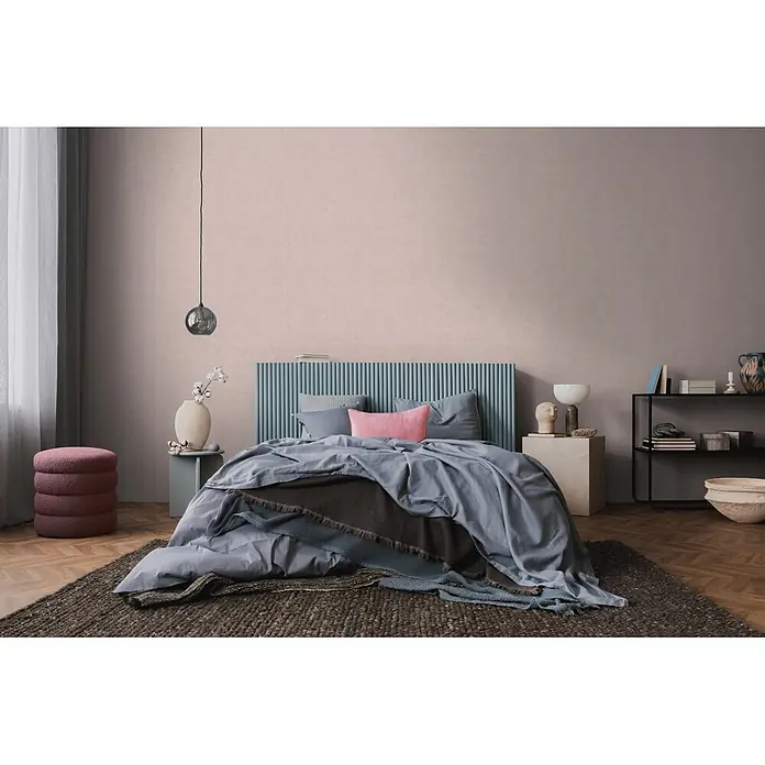 A.S. Création Nordic Feeling Vliestapete Uni - Grau-Lila, Uni, 10,05 x 0,53 m - Hellblaues und dunkelgraues Bettzeug mit rosa Akzentkissen auf einem Bett mit teal lamelliertem Kopfteil in einem modernen Schlafzimmer.
