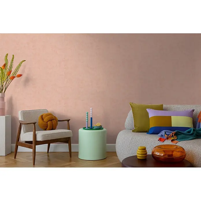 A.S. Création Nordic Feeling Vliestapete Uni - Rosa-Rot, Uni, 10,05 x 0,53 m - Strukturierte pfirsichfarbene Tapete bedeckt eine Wohnzimmerwand hinter Sessel und Sofa.