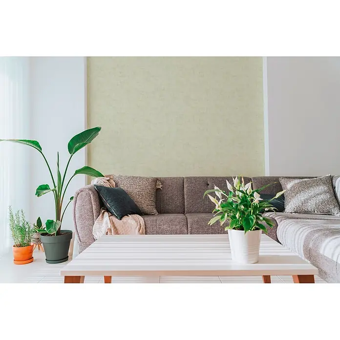 A.S. Création Nordic Feeling Vliestapete Uni I - Grün-Grau, Uni, 10,05 x 0,53 m - Ein braun-graues Stoffsofa mit texturierten Kissen und einem beigen Überwurf in einem Wohnzimmer.