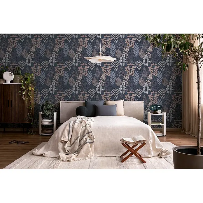 A.S. Création Nordic Feeling Vliestapete Blätter II - Blau-Lila, Uni, 10,05 x 0,53 m - Botanische Tapete in Blau-, Rosa- und Grautönen auf dunklem Hintergrund, über einem Bett im Schlafzimmer.