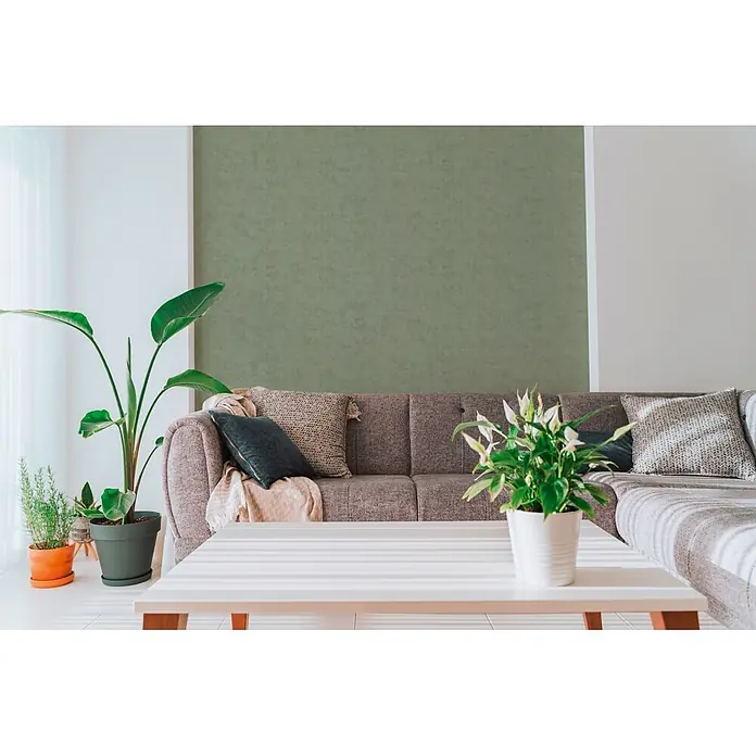 A.S. Création Nordic Feeling Vliestapete Uni - Dunkelgrün, Uni, 10,05 x 0,53 m - Modernes Wohnzimmer mit braunem Stoffsofa, Zierkissen, einem weißen Couchtisch und verschiedenen grünen Zimmerpflanzen für einen ruhigen Raum.