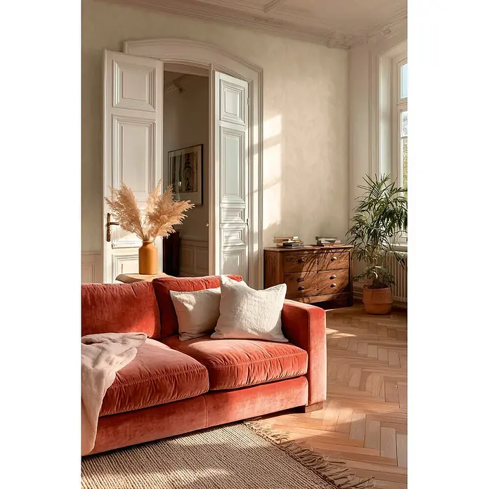 A.S. Création Metropolitan Stories Vibes & Styles Vliestapete Palme - Weiß, Floral, 10,05 x 0,53 m - Plüschiges korallenrotes Samtsofa mit hellen Kissen in einem sonnigen Wohnzimmer.
