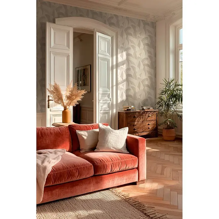 A.S. Création Metropolitan Stories Vibes & Styles Vliestapete Palme - Weiß-Beige, Floral, 10,05 x 0,53 m - Ein plüschiges korallenrotes Samtsofa mit hellen Kissen und einer rosa Decke in einem sonnigen Wohnzimmer.