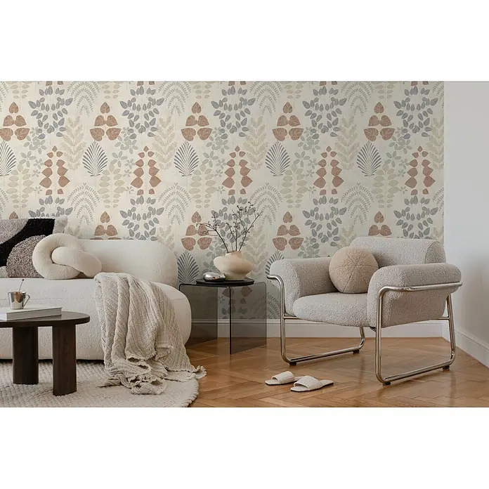 A.S. Création Nordic Feeling Vliestapete Blätter II - Beige-Braun, Uni, 10,05 x 0,53 m - Botanische Mustertapete in gedeckten Braun-, Blau- und Beigetönen an einer Wohnzimmerwand hinter einem cremefarbenen Sofa und einem hellgrauen Sessel.