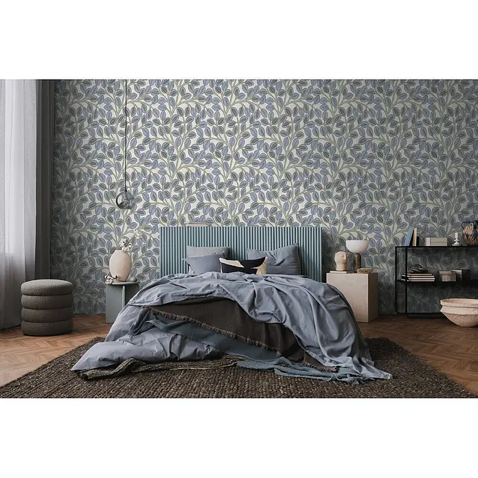 A.S. Création Nordic Feeling Vliestapete Blätter - Blau-Grau, Uni, 10,05 x 0,53 m - Blau-grüne Blättermuster-Tapete an einer Schlafzimmerwand, hinter einem Bett mit blauem Kopfteil und Bettwäsche.