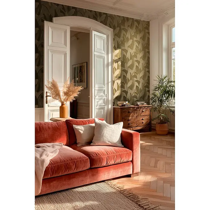 A.S. Création Metropolitan Stories Vibes & Styles Vliestapete Palme - Beige-Grün, Floral, 10,05 x 0,53 m - Korallenrotes Samtsofa mit hellen Kissen in einem sonnigen Wohnzimmer mit Teppich und botanischer Tapete.