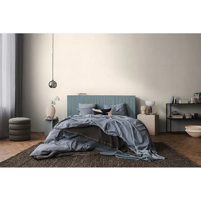 A.S. Création Nordic Feeling Vliestapete Uni - Creme-Weiß, Uni, 10,05 x 0,53 m - Texturierte hellbeige Wandverkleidung in einem stilvollen Schlafzimmer, schafft eine weiche, einladende Atmosphäre mit blauem Kopfteil und Bett.