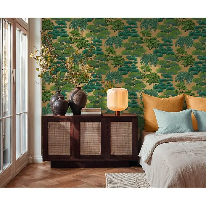 A.S. Création Cuba 2 Vliestapete Natur - Gold-Grün, Floral, 10,05 x 0,53 m - Dunkler Nachttisch aus Holz mit Rattan-Paneelen, darauf Vasen und eine Lampe, neben einem Bett.