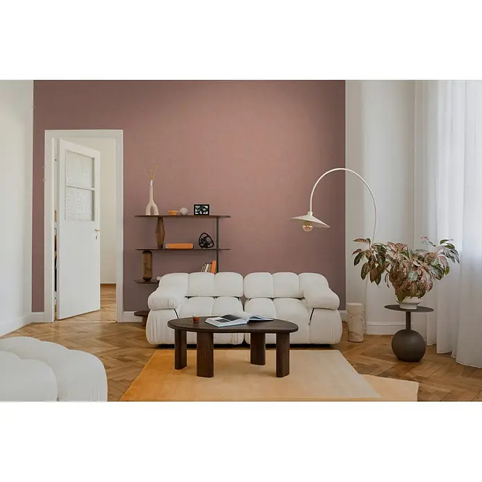 A.S. Création Nordic Feeling Vliestapete Uni - Braun-Rot, Uni, 10,05 x 0,53 m - Ein weißes, modulares, strukturiertes Sofa in einem Wohnzimmer, platziert auf einem orangefarbenen Teppich vor einer rotbraunen Wand.