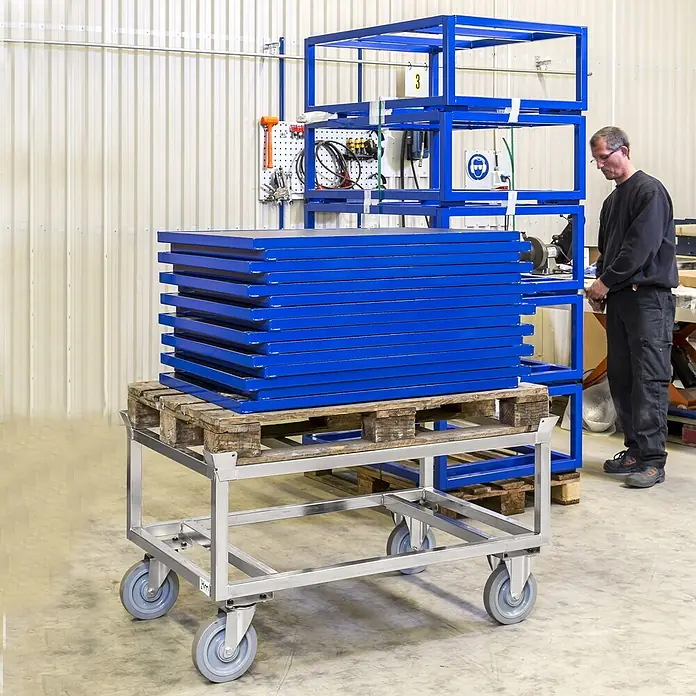 Kongamek Palettenwagen Palettenwagen verzinkt und verschweißt, höhenverstellbar 700mm hoch mit B -  - Silberner Industrietrolley mit Rollen, der eine Palette gestapelter blauer Metallteile in einer Fabrik trägt.