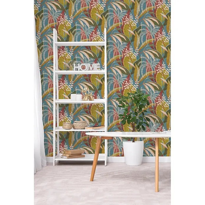 A.S. Création Pintwalls 3 Vliestapete Tropen - Blau-Rot, Floral, 10,05 x 0,53 m - Botanische Mustertapete mit großen Blättern in Petrol, Rot, Grün, Gelb und Beige, an einer Wand in einem modernen Raum angebracht.