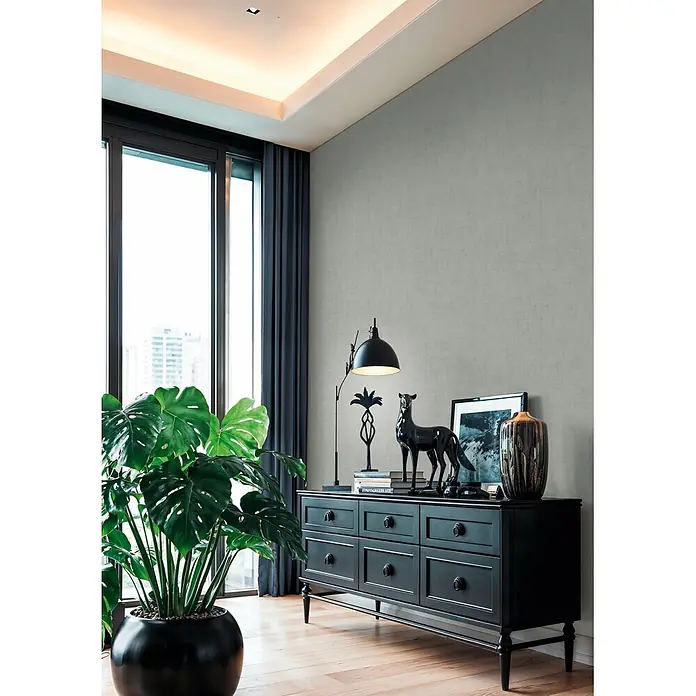 A.S. Création Cuba 2 Vliestapete Uni - Grün-Grau, Uni, 10,05 x 0,53 m - Moderner Wohnraum mit großer Monstera-Pflanze in schwarzem Topf und schwarzem Sideboard unter einem Fenster.