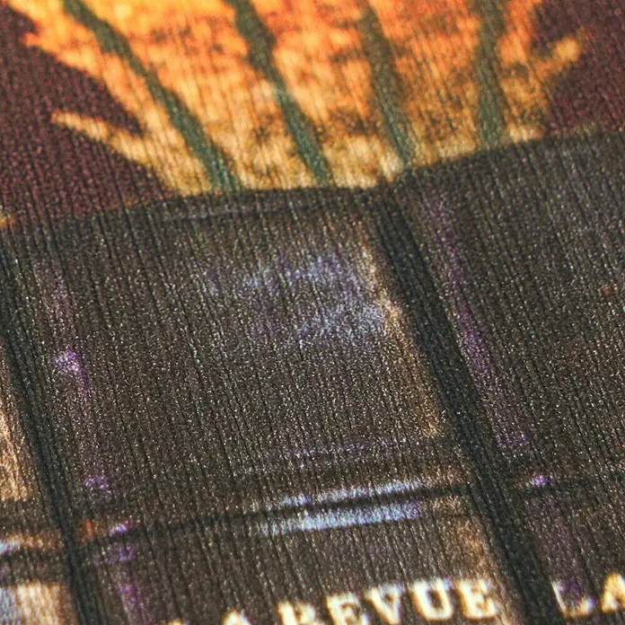 A.S. Création Pintwalls 3 Vliestapete Bücher - Grün-Braun, Sonstiges, 10,05 x 0,53 m - Nahaufnahme eines bedruckten Stoffes: Texturierte dunkle Linien mit violetten Akzenten und Teilschriftzug „REVUE LA“. Oben warme Orange-Töne.