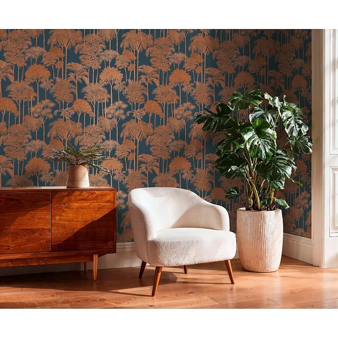A.S. Création Cuba 2 Vliestapete Wald - Blau-Braun, Floral, 10,05 x 0,53 m - Ein cremefarbener Stoff-Sessel mit Holzbeinen steht auf Holzboden neben einer großen Pflanze und einem Holzschrank in einem Raum mit gemusterter Tapete.