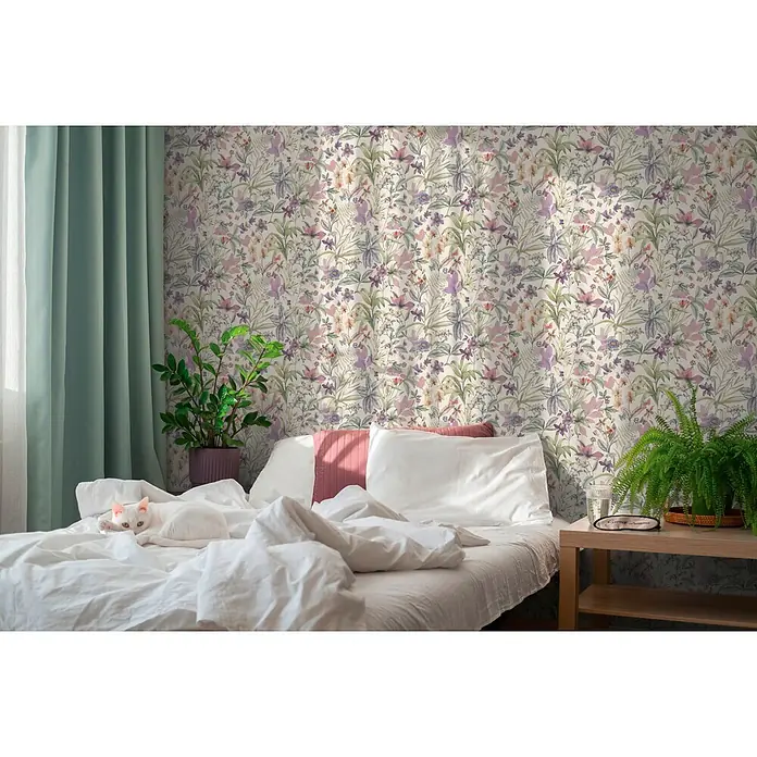 A.S. Création Pintwalls 3 Vliestapete Blüten - Weiß-Lila, Floral, 10,05 x 0,53 m - Blumige Tapete in Lila, Rosa und Grün auf hellem Hintergrund, schmückt eine Schlafzimmerwand hinter Bett und Pflanzen.