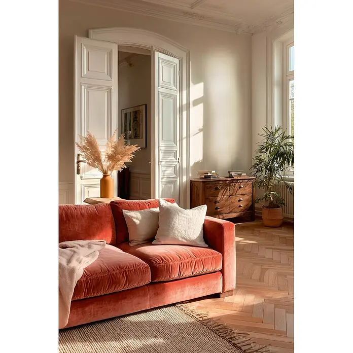A.S. Création Metropolitan Stories Vibes & Styles Vliestapete Textil - Creme, Uni, 10,05 x 0,53 m - Korallenrotes Samtsofa mit Decke und Kissen in einem sonnigen Wohnzimmer.