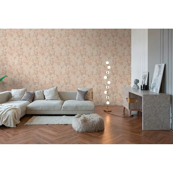 A.S. Création Pintwalls 3 Vliestapete Blüte - Creme-Orange, Floral, 10,05 x 0,53 m - Helle, floral gemusterte Tapete mit Pastellrosenmotiven an einer Wohnzimmerwand hinter einem Sofa.
