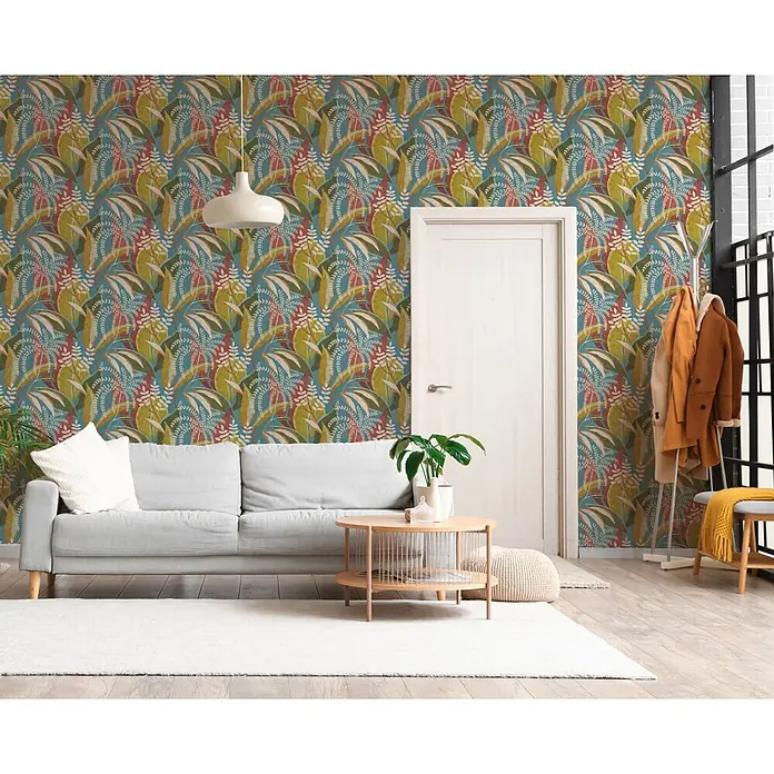 A.S. Création Pintwalls 3 Vliestapete Tropen - Blau-Rot, Floral, 10,05 x 0,53 m - Botanische Tapete mit lebhaftem Muster aus grünen, roten und gelben Blättern auf blauem Hintergrund, in einem modernen Wohnzimmer.