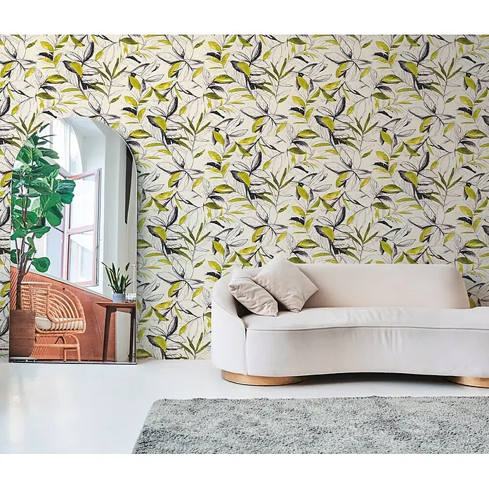 A.S. Création Pintwalls 3 Vliestapete Blätter - Grün-Schwarz, Floral, 10,05 x 0,53 m - Tapete mit grünem und schwarzem gezeichnetem Blattmuster, bedeckt eine Wand in einem hellen Wohnzimmer, mit hellem Sofa und Spiegel im Vordergrund.