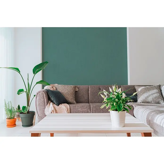 A.S. Création Cuba 2 Vliestapete Uni - Grün-Blau, Uni, 10,05 x 0,53 m - Moderne Wohnzimmer mit einer strukturierten, petrolfarbenen Akzentwand hinter einem grauen Sofa.