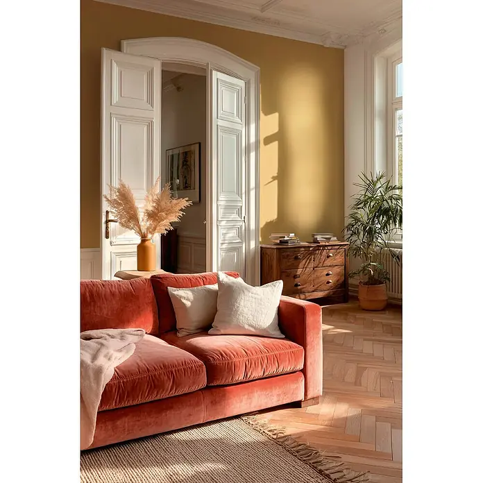 A.S. Création Metropolitan Stories Vibes & Styles Vliestapete Textil - Gelb, Uni, 10,05 x 0,53 m - Ein plüschiges korallenfarbenes Samtsofa mit hellen Kissen in einem sonnigen Wohnzimmer, das Komfort bietet.