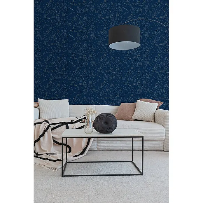 A.S. Création Pintwalls 3 Vliestapete Gesichter - Blau-Gold, Grafisch, 10,05 x 0,53 m - Dunkelblaue Tapete mit goldenem abstraktem Gesichts-Linienmuster an einer Wohnzimmerwand hinter einem Sofa.