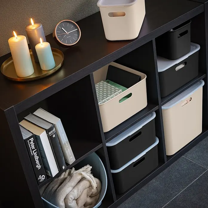 Sunware Sigma home Aufbewahrungsbox cube box - L x B x H: 31 x 31 x 31 cm, Kunststoff, Beige, 25 l - Dunkles Regal gefüllt mit beigefarbenen und schwarzen Aufbewahrungsboxen, Büchern, Kerzen und einer Uhr, bietet organisierte Aufbewahrung.