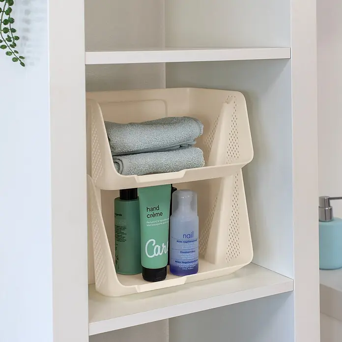 Sunware Sigma home Schreibtisch-Organizer Stackable - L x B x H: 20 x 25 x 17,5 cm, Beige, Kunststoff - Zwei stapelbare, beigefarbene Kunststoff-Aufbewahrungskörbe mit Lochmuster, gefüllt mit blauen Handtüchern und Toilettenartikeln in einem Regal.