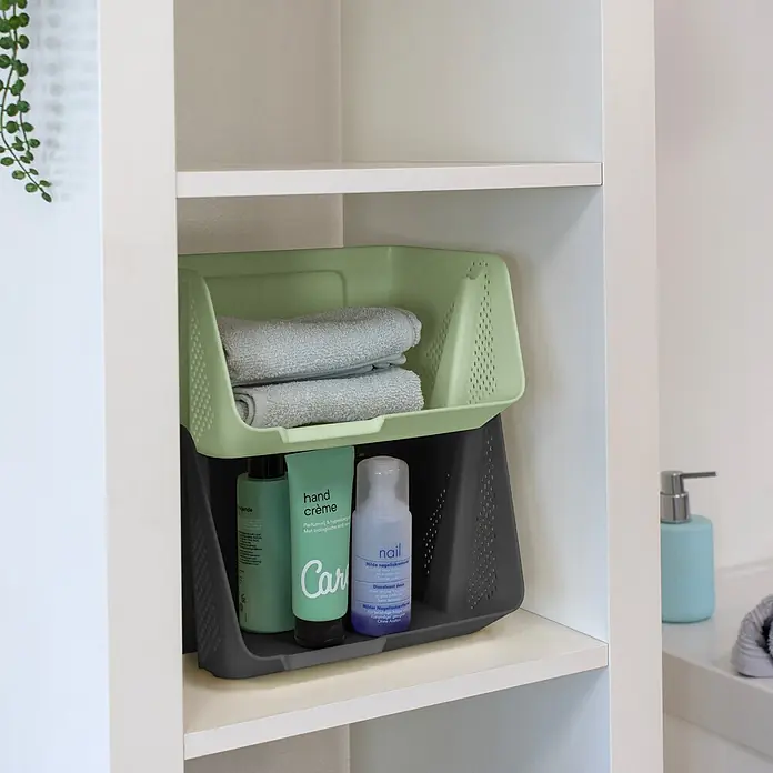 Sunware Sigma home Schreibtisch-Organizer Stackable - L x B x H: 20 x 25 x 13 cm, Grün, Kunststoff - Zwei stapelbare Kunststoff-Aufbewahrungskörbe, hellgrün und dunkelgrau, mit Handtüchern und Toilettenartikeln in einem weißen Schrank.