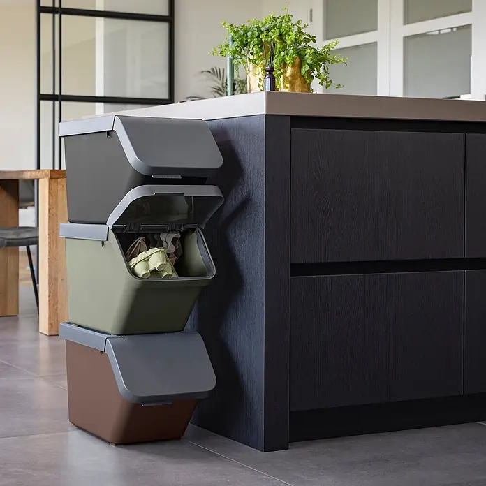 Sunware Sigma home Mülltrennsystem - 60 l, L x B x H: 49,3 x 38,8 x 44,8 cm, Anthrazit, Kunststoff - Drei stapelbare Recyclingbehälter in Dunkelgrau, Olivgrün und Braun neben einer Kücheninsel. Der mittlere Behälter ist geöffnet, mit Papiermüll.
