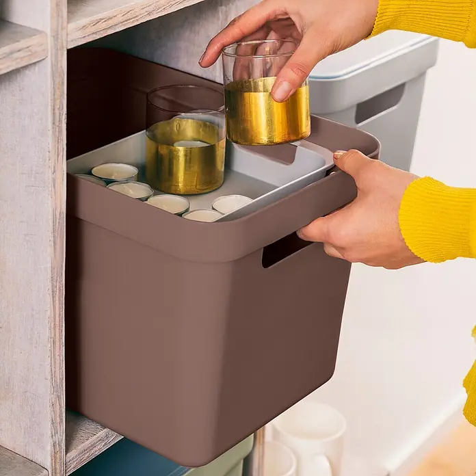Sunware Sigma home Aufbewahrungsbox - L x B x H: 35 x 24,6 x 24,3 cm, Kunststoff, Schoko - Braune Aufbewahrungsbox wird in ein Holzregal gestellt, enthält Teelichter und goldene Kerzenhalter.