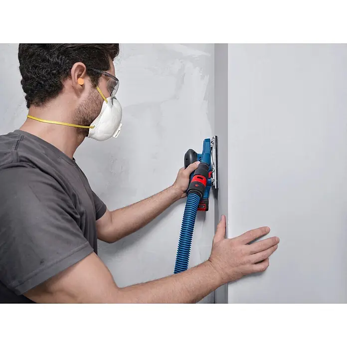 Bosch Professional AMPShare 18V Akku-Schwingschleifer - Anzahl Akkus: Ohne Akku, 10.000 U/min - 20.000 U/min, 18 V, Koffer - Person schleift eine Wand mit blau-schwarzem Elektroschleifer und Absaugschlauch.