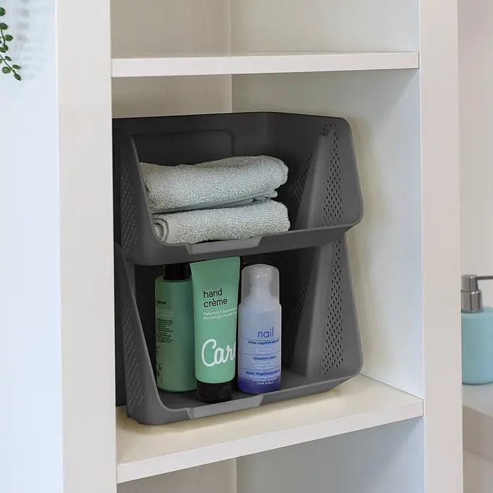 Sunware Sigma home Schreibtisch-Organizer Stackable - L x B x H: 20 x 25 x 17,5 cm, Anthrazit, Kunststoff - Grau gestapelte Kunststoff-Aufbewahrungskörbe auf einem weißen Regal, gefüllt mit Handtüchern und Pflegeprodukten.