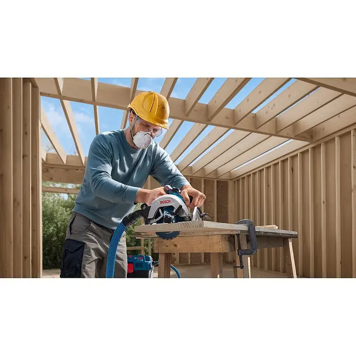 Bosch Professional AMPShare 18V Akku-Handkreissäge GKS 18V-68-2 SOLO - 19 V, Ohne Akku, Durchmesser Sägeblatt: 190 mm, 5.225 U/min - 5.775 U/min - Eine Person sägt mit einer weißen, blauen Bosch Handkreissäge Sperrholz auf einer Baustelle, verbunden mit einem Staubsauger.
