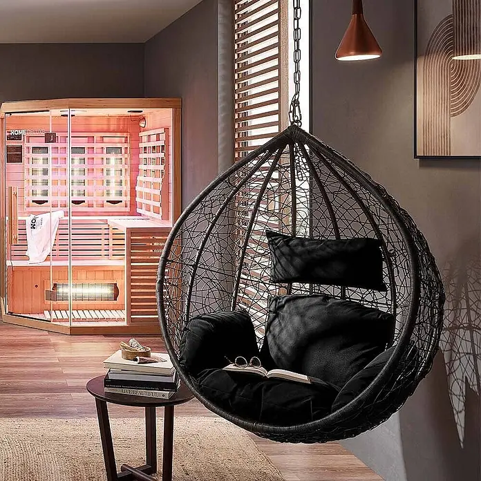 Home Deluxe Hängesessel CIELO - L x B x H: 104 x 104 x 200 cm, Schwarz - Schwarzer Hängesessel aus Korbgeflecht mit Kissen und eine Infrarotsauna aus Holz in einem modernen Raum.