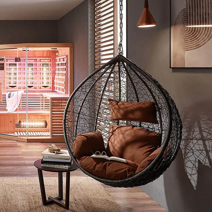Home Deluxe Hängesessel CIELO Korb - Kunststoff, Grau - Schwarzer Hängesessel mit weichen braunen Kissen, in einem gemütlichen Raum neben einer Sauna.