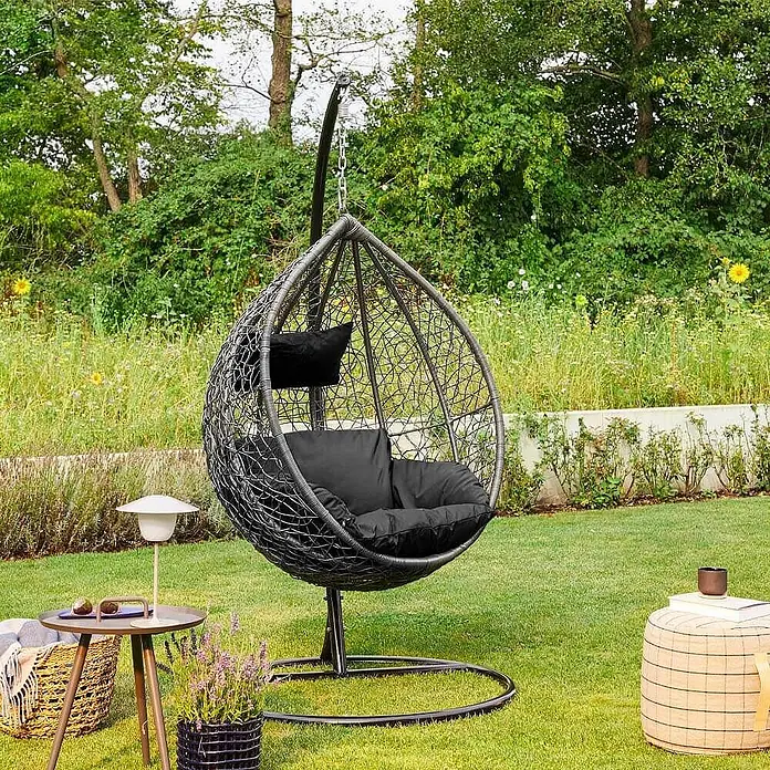 Home Deluxe Hängesessel CIELO - L x B x H: 104 x 104 x 200 cm, Schwarz - Dunkelgrauer geflochtener Hänge-Eiersessel mit schwarzen Kissen, auf einem Ständer im Freien.