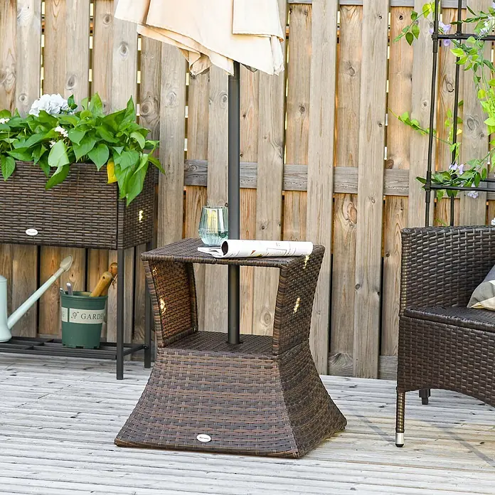 Outsunny Garten-Beistelltisch - L x B x H: 54 x 54 x 55 cm, Metall, Polyrattan, Quadratisch, Braun - Brauner Rattantisch für den Außenbereich mit integriertem Sonnenschirmständer, auf dem ein Getränk und eine Zeitschrift liegen.