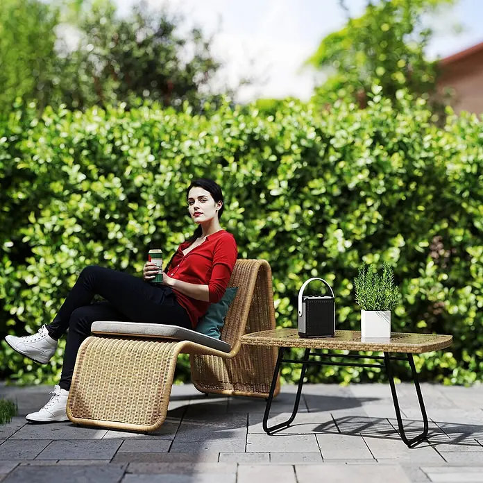 Outsunny Garten-Beistelltisch - L x B x H: 90 x 50 x 45 cm, Stahl, PE-Rattan, gehärtetes Glas, Rechteckig, Naturholz - Frau entspannt sich in einem geflochtenen Rattansessel mit Kissen im Garten. Hellbraun, natürliche Textur.