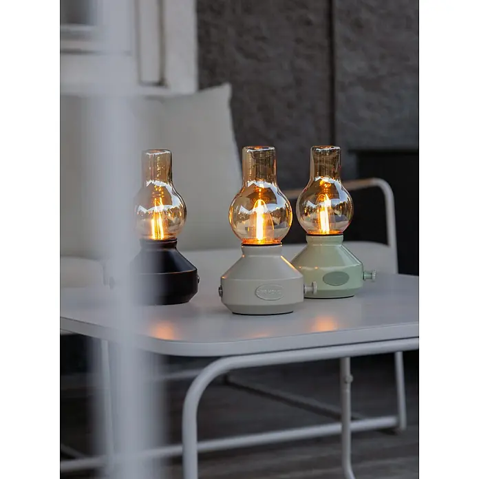 PR Home Akku-Tischleuchte schwarz Outdoor - Warmweiß, 1 W - Drei tragbare Lampen (Schwarz, Beige, Hellgrün) mit leuchtenden Bernsteinbirnen auf einem Gartentisch.