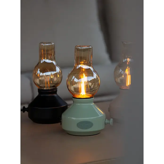 PR Home Akku-Tischleuchte schwarz Outdoor - Warmweiß, 1 W - Drei Retro-Tischlampen mit bernsteinfarbenen Glasbirnen auf Holztisch. Schwarz, mintgrün, hellgrau, alle leuchtend, spenden warmes Licht.