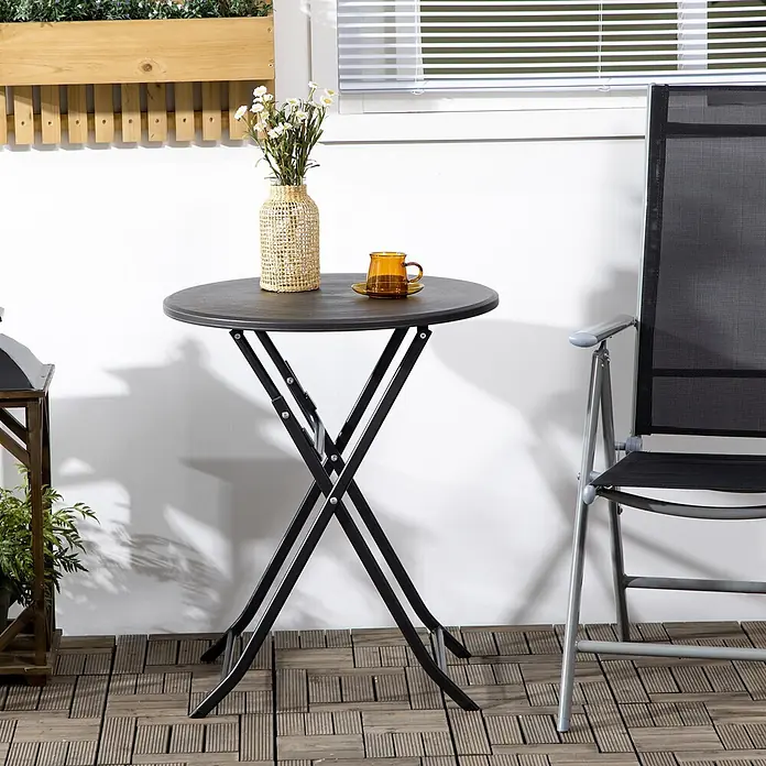 Outsunny Balkontisch rund mit Holzoptik - Stahl, HDPE-Kunststoff, Klappbar, Dunkelgrau - Runder, dunkler Klapptisch mit schwarzen Metallbeinen, gezeigt mit Stuhl, Blumen und Tasse auf einer Terrasse.