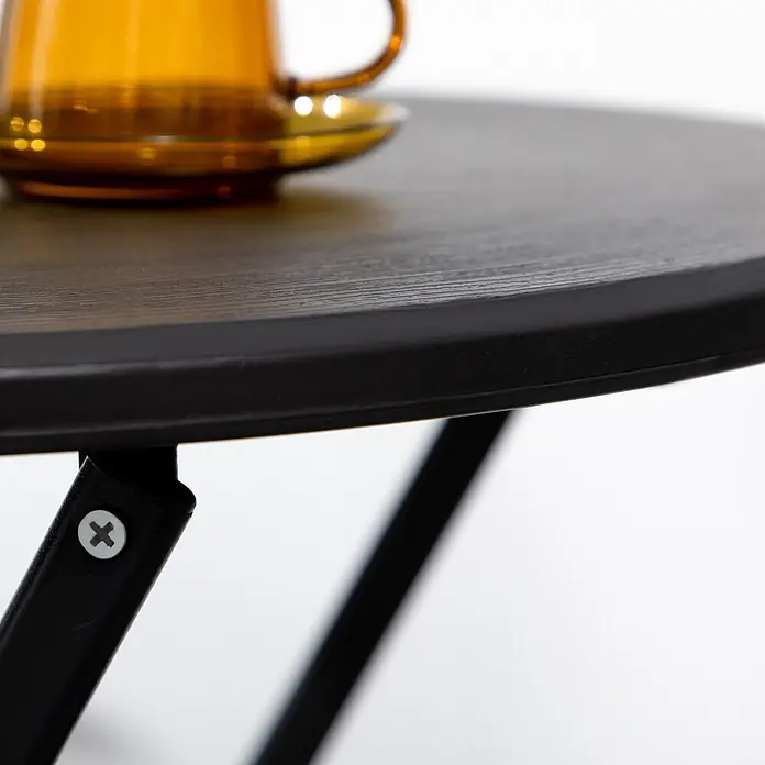 Outsunny Balkontisch rund mit Holzoptik - Stahl, HDPE-Kunststoff, Klappbar, Dunkelgrau - Runder Klapptisch mit dunkler Holzoptik und schwarzen Metallbeinen. Eine unscharfe bernsteinfarbene Tasse steht auf der strukturierten Oberfläche.