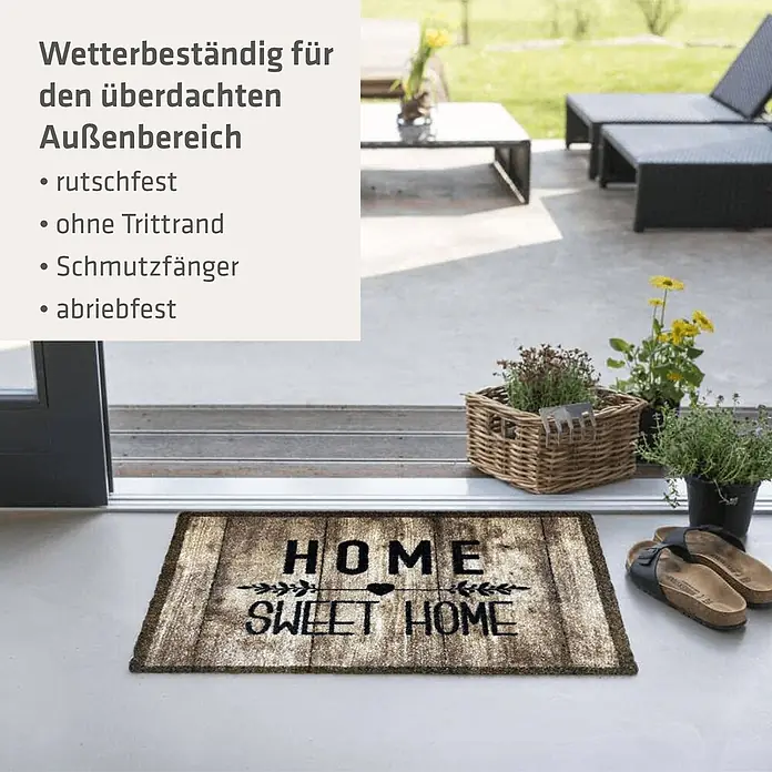 Akzente Fußmatte Listen - Mehrfarbig, Schriftzug - Braune "HOME SWEET HOME" Fußmatte auf einer Terrasse vor einer Glastür, mit Hausschuhen und Pflanzen.