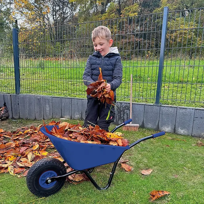 Pro-Bau-Tec Bollerwagen Kinderschubkarre Blau mit PP-Mulde 20L mit PU-Rad - L x B x H: 1,05 cm x 0,34 cm x 0,39 m - Ein Kind füllt eine blaue Garten-Schubkarre mit Herbstlaub. Sie hat eine blaue Wanne und einen schwarzen Rahmen.