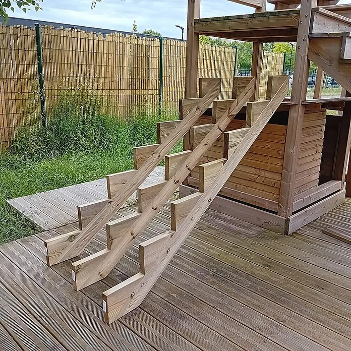 Vinuovo Außentreppe 3er Set Treppenwange 7 Stufen aus KDI Holz für Gartentreppen-Höhe 119cm - Anzahl Steigungen: 7 Stk., Gerade - Helle Holztreppe auf einer Holzterrasse, die zu einem Spielhaus führt, umgeben von Zaun und Gras.