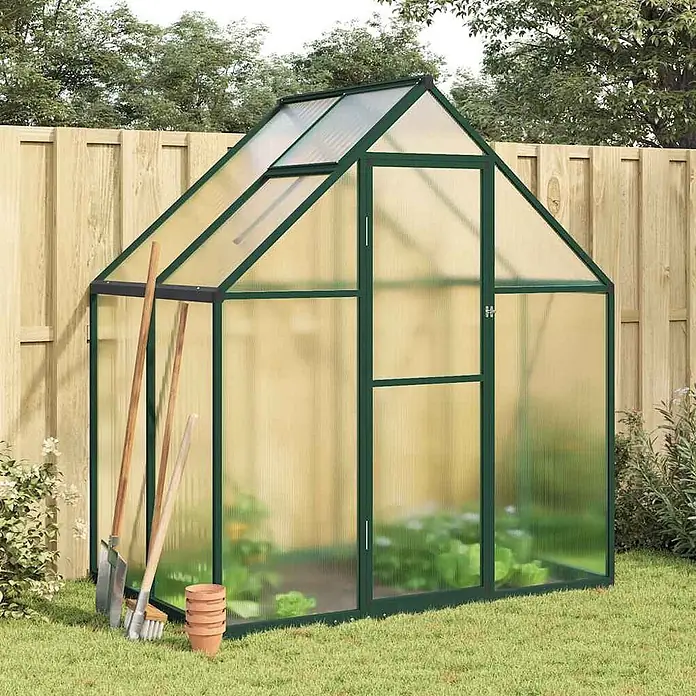 Furnicato Gewächshaus - Außenmaß inkl. Dachüberstand (B x T): 114 x 169 cm, Material Seitenwand: Aluminium, 0,4 mm, Grün - Dunkelgrünes Gewächshaus mit lichtdurchlässigen Paneelen, A-Dach und Dachfenster, im Garten mit wachsenden Pflanzen.