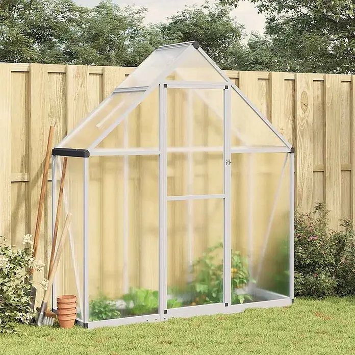 Furnicato Gewächshaus - Außenmaß inkl. Dachüberstand (B x T): 58 x 169 cm, Material Seitenwand: Aluminium, 0,4 mm, Silbern - Ein freistehendes Gewächshaus mit silbernem Aluminiumrahmen und transparenten Polycarbonatplatten, im Garten mit Pflanzen.