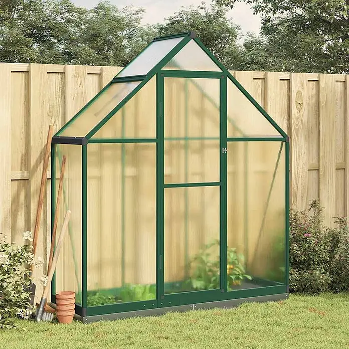 Furnicato Gewächshaus - Außenmaß inkl. Dachüberstand (B x T): 58 x 169 cm, Material Seitenwand: Aluminium, 0,4 mm, grün - Ein grün umrahmtes Gewächshaus mit durchscheinenden Platten steht in einem Garten neben einem Holzzaun, enthält Pflanzen und ist von Gartengeräten umgeben.